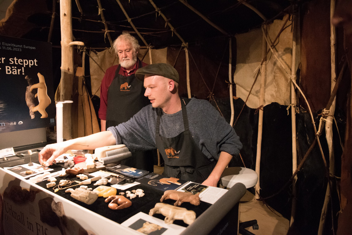 Elfenbeinschnitzer Bernhard Röck und Louis Corrigan in ihrem Handwerkerzelt in der Ausstellung &quot;Eiszeit Safari Allgäu&quot;